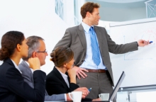 Man pointing at a flip chart with three colleagues watching him.