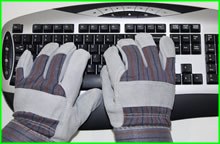 A person wearing thick gloves trying to type on a computer keyboard.