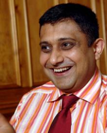 Photograph of Sanjay Morzaria wearing an orange and white stripped shirt.