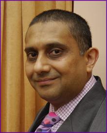 Sanjay Morzaria head photo wearing a purple checked shirt, tie and suit jacket.